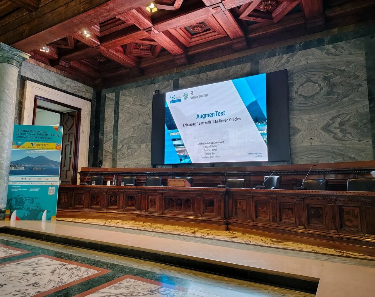 The AugmenTest title slide on the screen of a frescoed hall at ICST 2025 in Naples.